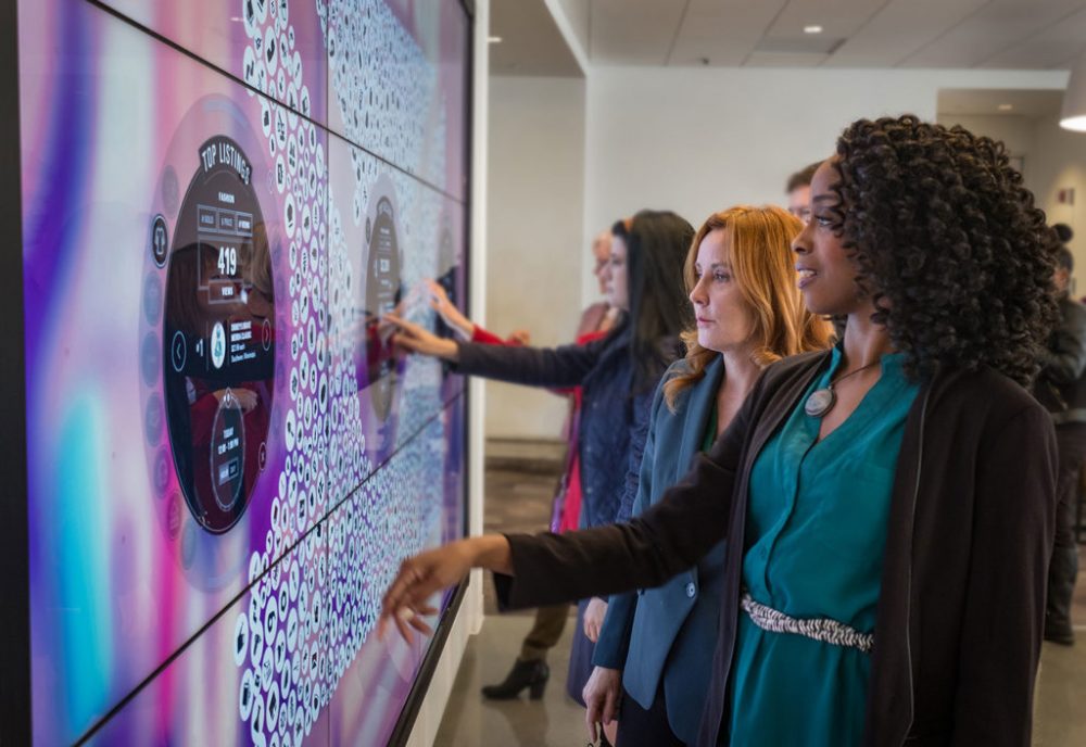 People point at a large touch screen.