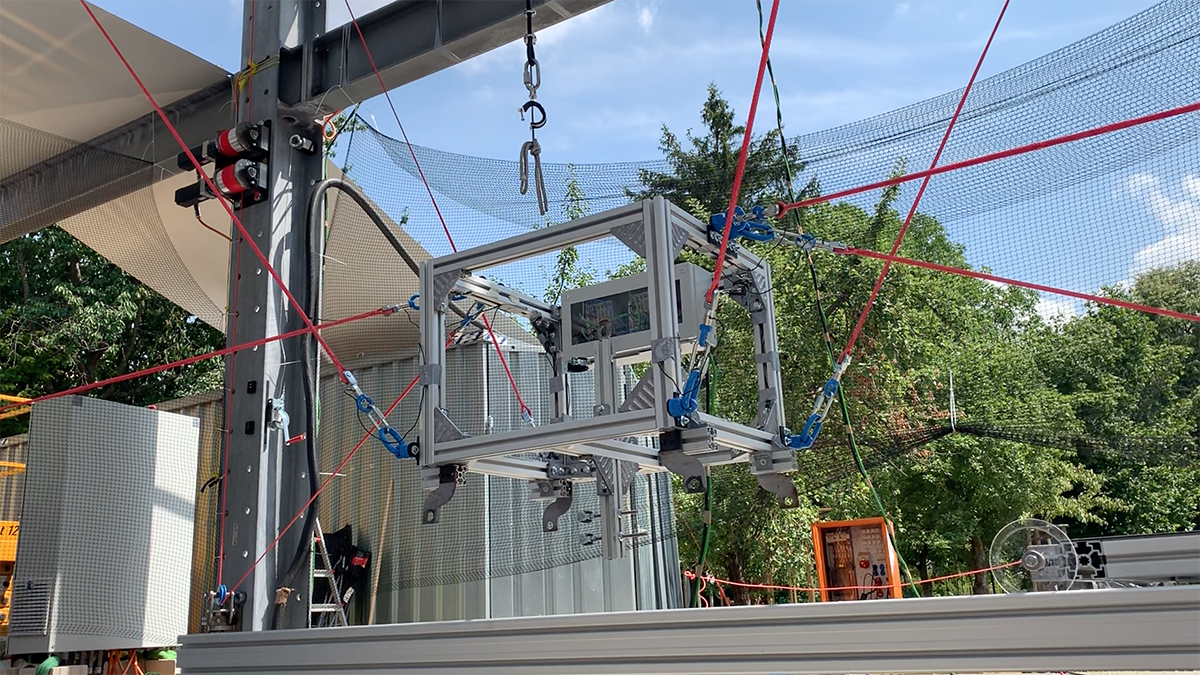 A robot in the form of a metal box is attached to various red cables and suspended a few feet in the air, unveiled for the Bauhaus centennary