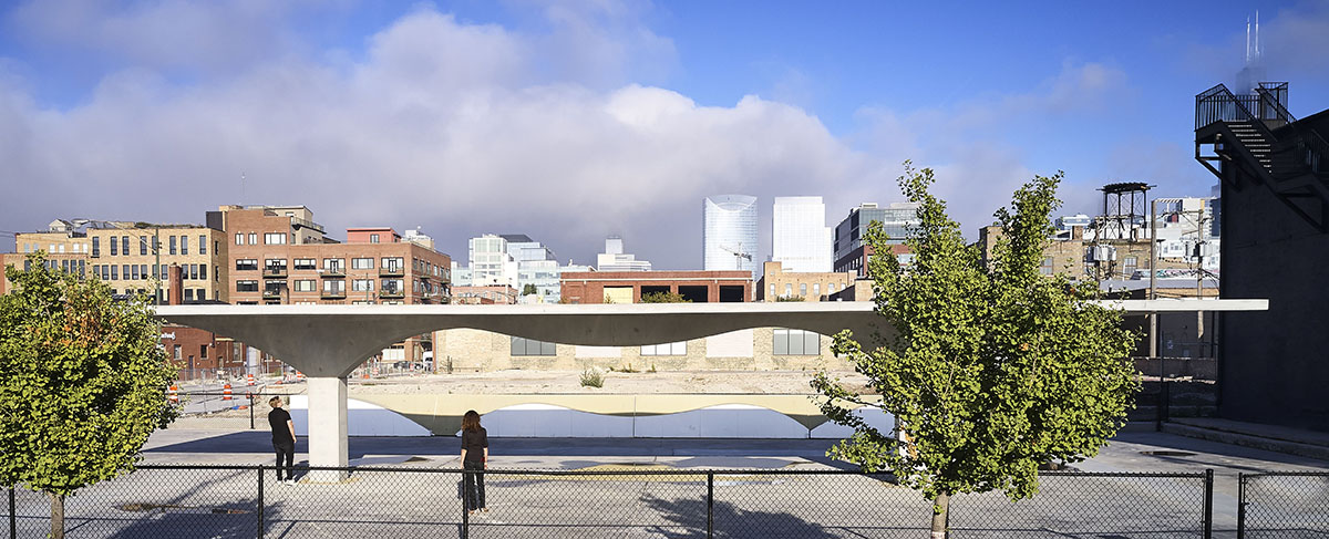 A wide angle shot of a concrete roof structure foregrounded with trees and with the city in the background.